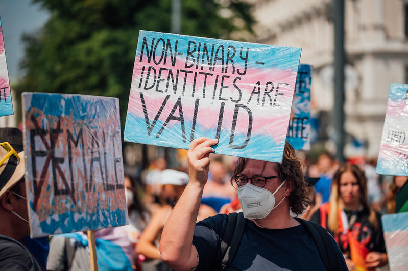 A protestor wearing a facemask and carrying a placard that reads 'Non-binary identities are valid'.
