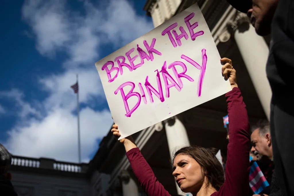 A person holding a poster that reads: Break the binary.