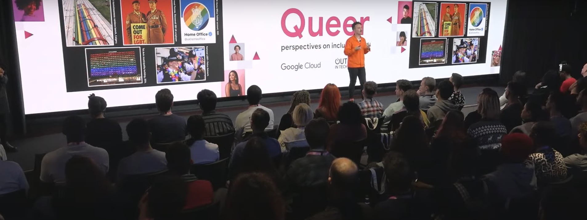 Kevin standing on a stage at a Google Cloud event. He is wearing an orange jacket and black jeans. On the screen behind it says: Queer perspectives on inclusive data.